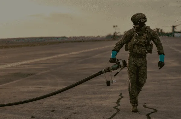 Soldier carrying a fuel line across a tarmac at an airfield