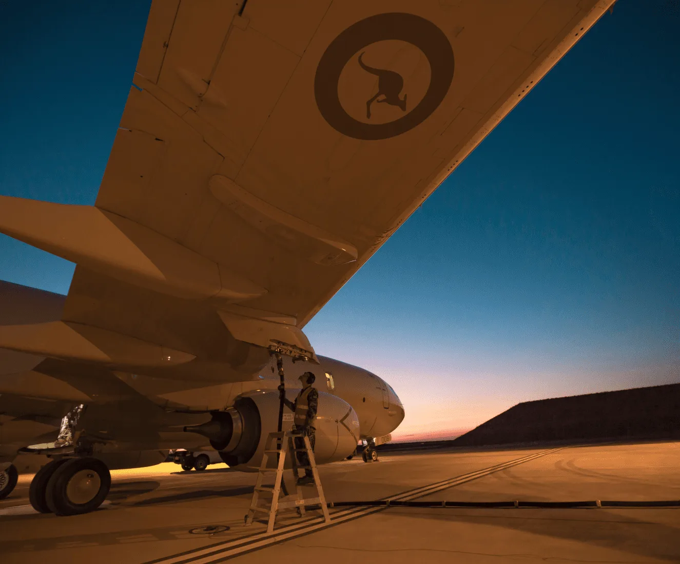 Technician monitors a fuel line connected to the wing of an aircraft, at dawn on a tarmac